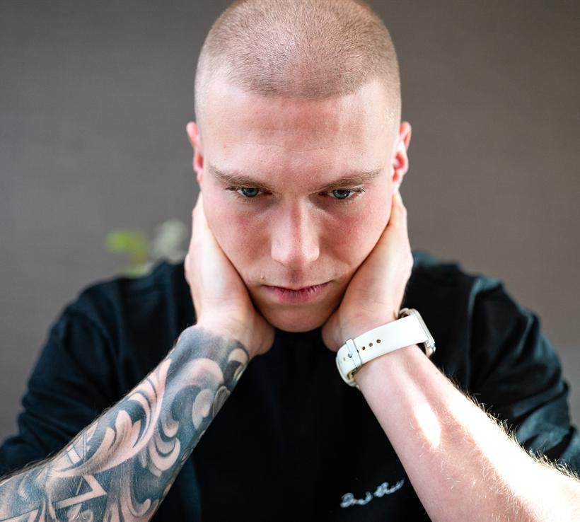 Jonge man met zijn handen in zijn nek, blik omlaag